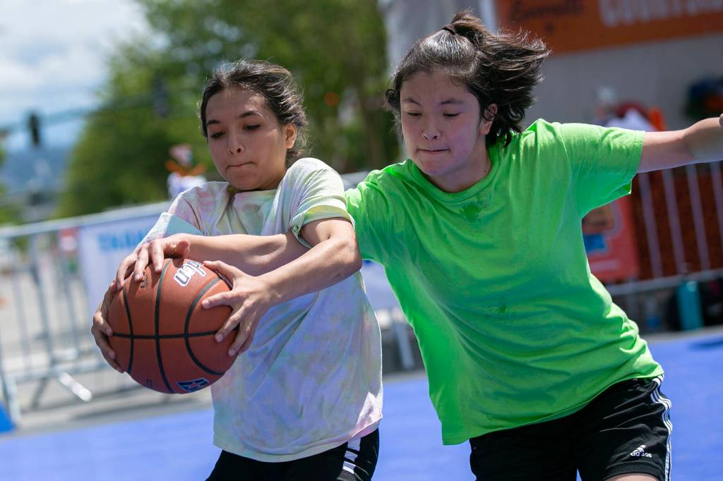 Two players chase down a ball while playing at Center Court during Everett 3on3 Saturday, July 9, 2022, in downtown Everett, Washington. (Ryan Berry / The Herald)
