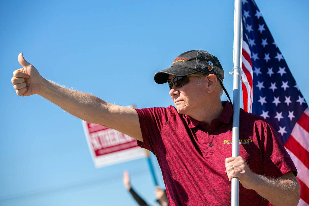 State Representative Robert Sutherland, who is seeking re-election in the 39th District this year, gives a thumbs-up to passing drivers as he and a few volunteers wave flags and campaign signs along the side of State Route 9 on Friday, in Lake Stevens. (Ryan Berry / The Herald)