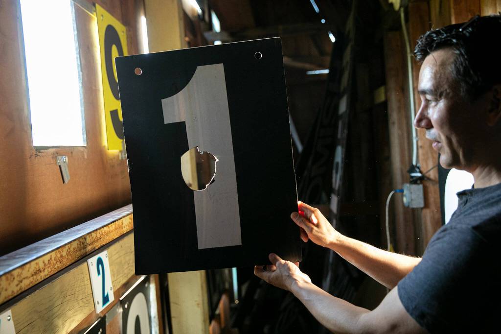 Nick Patterson holds up a tile that at some point was struck by a fly ball to the wall on Saturday, July 23, 2022, inside the outfield scoreboard at Funko Field in Everett, Washington. (Ryan Berry / The Herald)