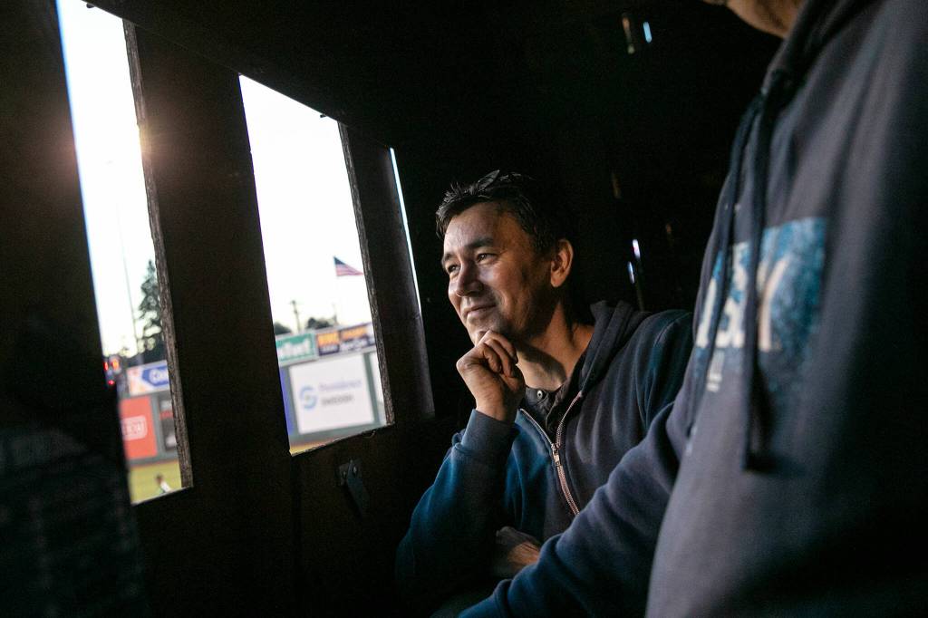 Everett Herald sports reporter Nick Patterson stands alongside first-year scoreboard operator Craig Hancock and watches the AquaSox game on Saturday, July 23, 2022, inside the outfield scoreboard at Funko Field in Everett, Washington. (Ryan Berry / The Herald)