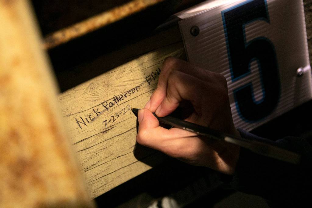 Nick Patterson signs his name after a successful night of tending to the manual scoreboard on Saturday, July 23, 2022, at Funko Field in Everett, Washington. (Ryan Berry / The Herald)