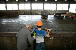 Twenty-four-year-old Joel Christensen, who was born with Infantile Refsum disease, causing him to be unable to see or fully hear, stands with his grandfather Harold at his side as he tosses trash into the pit at the the Airport Road Transfer Station on Thursday, Aug. 4, 2022, in Everett, Washington. Going to the transfer station is one of Joel’s favorite activities with the vibration of humming machinery, the whooshing of front end loaders and the tactile nature of his family’s trash all stimulating his strongest senses. (Ryan Berry / The Herald)