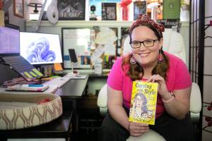 Erika Weinert, an Everett-based mother, editor and now author, sits at her home workspace and holds her first published book, “Cursing with Style” on Saturday, Aug. 6, 2022, in Everett, Washington. (Ryan Berry / The Herald)