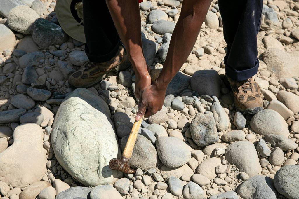 Don Smith uses a hammer to pry away rocks from a large specimen of olivine on July 23 along the Nooksack River near Deming. (Ryan Berry / The Herald)