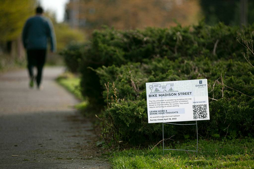 A pedestrian walks along the Interurban Trail and past a sign asking for public input on proposed bike lanes on Madison Street on April 14, in Everett. (Ryan Berry / The Herald)
