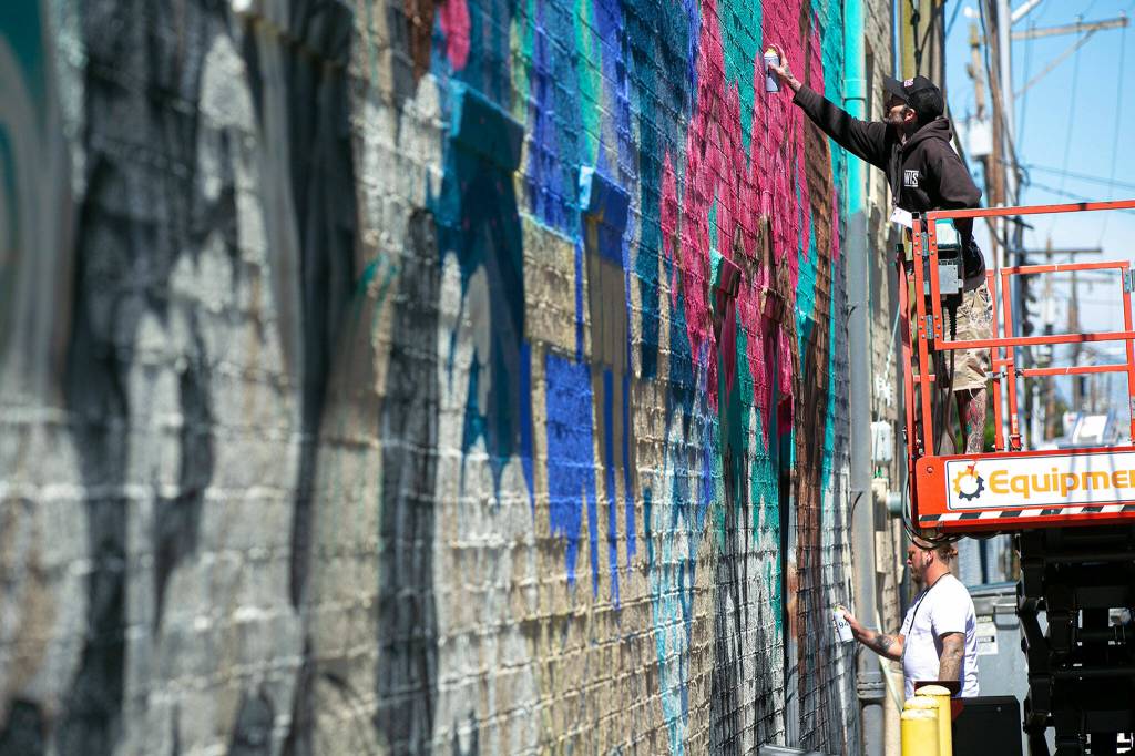 Everett artist Shisha, above, and Karoe of Tyler, Texas, work on a full-building mural together on Friday, in downtown Everett. (Ryan Berry / The Herald)
