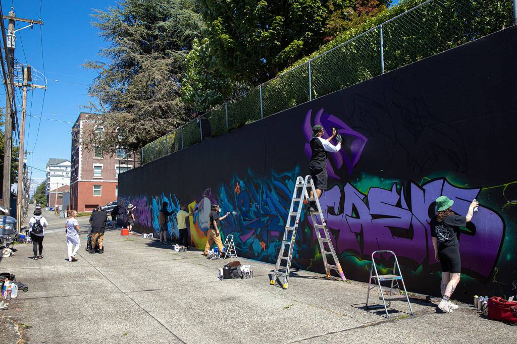 More than half a dozen artists come together to put their mark on an alley wall on Friday, in downtown Everett. Many passersby took a moment to swing through the alley and ask questions about Going All City NW. (Ryan Berry / The Herald)