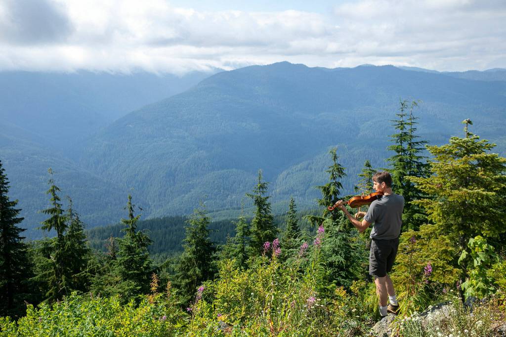 Carson Tavenner plays his viola while looking out over the mountains on Wednesday, Aug. 10, at the North Mountain Fire Lookout north of Darrington. (Ryan Berry / The Herald)