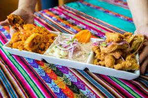 Co-owner of Rinconcito Peruano Restaurant Genesis Rojas brings out a Triple Marino dish that consists of arroz con mariscos, ceviche and jalea mixta on Saturday, Aug. 13, 2022 in Lynnwood, Washington. (Olivia Vanni / The Herald)