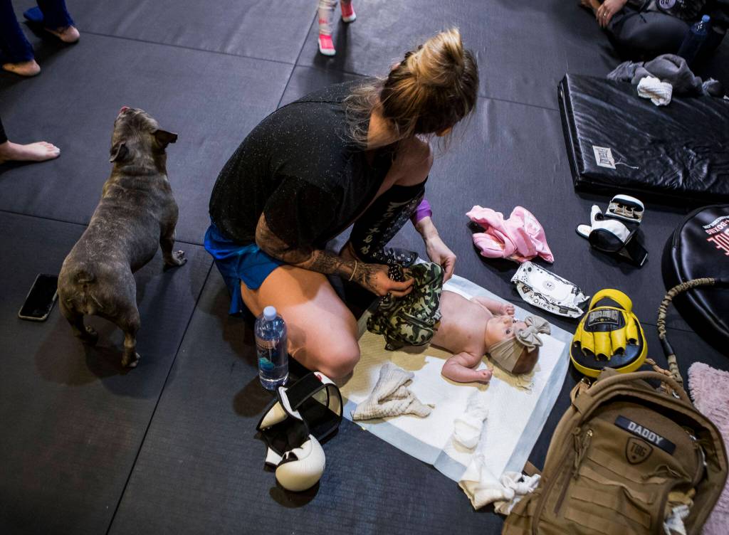 Before a workout class, Miranda Granger changes her daughters diaper on the floor of Charlies Combat Club on Nov. 8, 2021, in Everett, Washington. Granger often brought Austin with her to the gym, along with a baby bag of items for diaper changes, toys, blankets and snacks. (Olivia Vanni / The Herald)