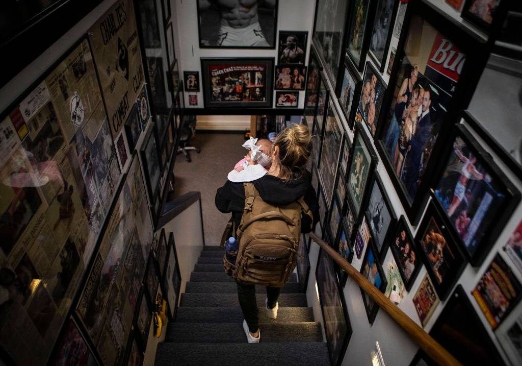 Miranda Granger holds Austin and walks down a hallway covered in photographs of fighters at Charlies Combat Club on Monday, Nov. 8, 2022, in Everett, Washington. (Olivia Vanni / The Herald)