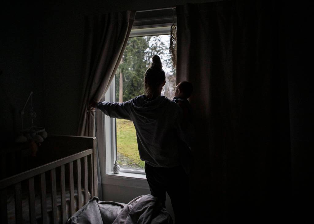 Miranda Granger holds her daughter Austin and reaches out to close the blinds for nap time on Monday, Feb. 28, 2022, in Lake Stevens, Washington. (Olivia Vanni / The Herald)