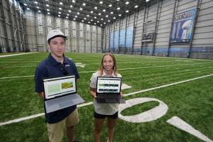Peter Engler, left, a football research assistant, and Becca Erenbaum, a senior football research analyst, hold laptop computers as they pose for a photo on Aug. 3, 2022 at the Seattle Seahawks' NFL football indoor training facility in Renton, Wash. Their job is to make sense of numbers and systems. They run code and develop programs and live in a world of language that if interpreted and translated correctly can be a differentiator between success and failure. (AP Photo/Ted S. Warren)