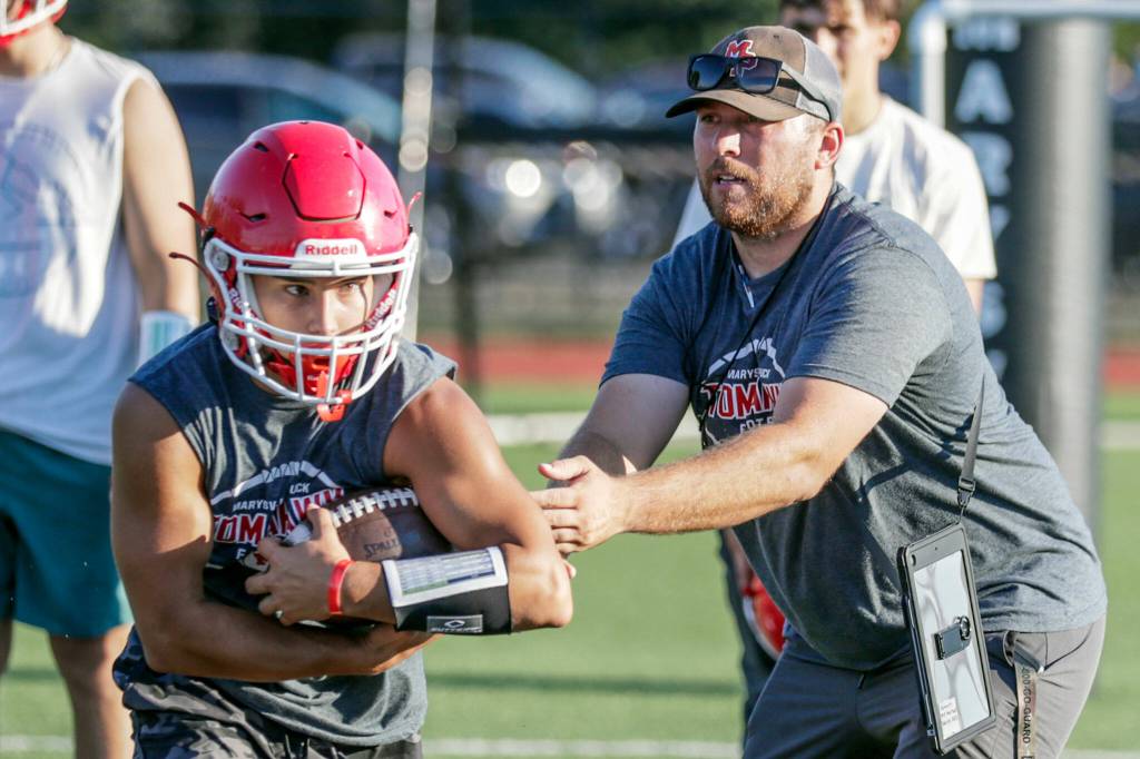Kenai Sinaphet takes the hand off from head coach Dalton Schwetz during practice Aug. 17 at Marysville Pilchuck High School in Marysville. (Kevin Clark / The Herald)