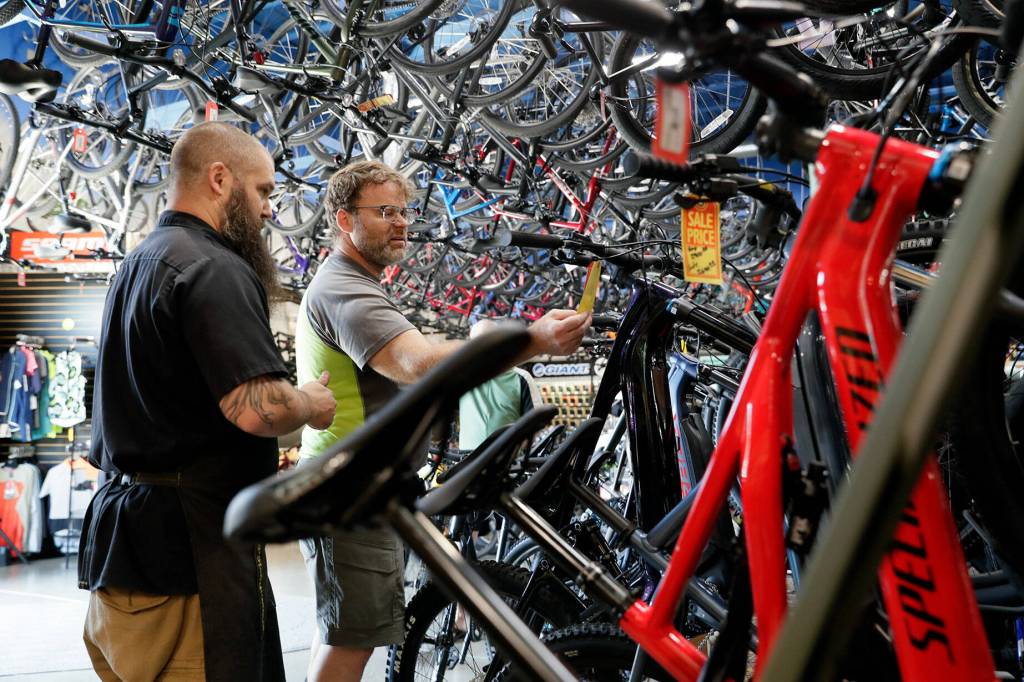 Devin Ryan, left, talks electric mountain bikes Donald Whitley at Bicycle Centres Wednesday in Everett, Washington on August 24, 2022. (Kevin Clark / The Herald)