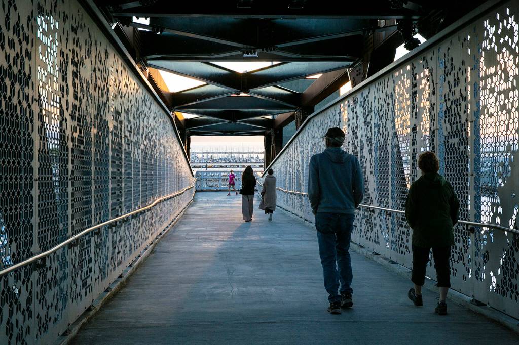 Pedestrians cross over Marine View Drive on the Grand Ave Park Bridge as the sun sets Wednesday, in Everett. (Ryan Berry / The Herald)