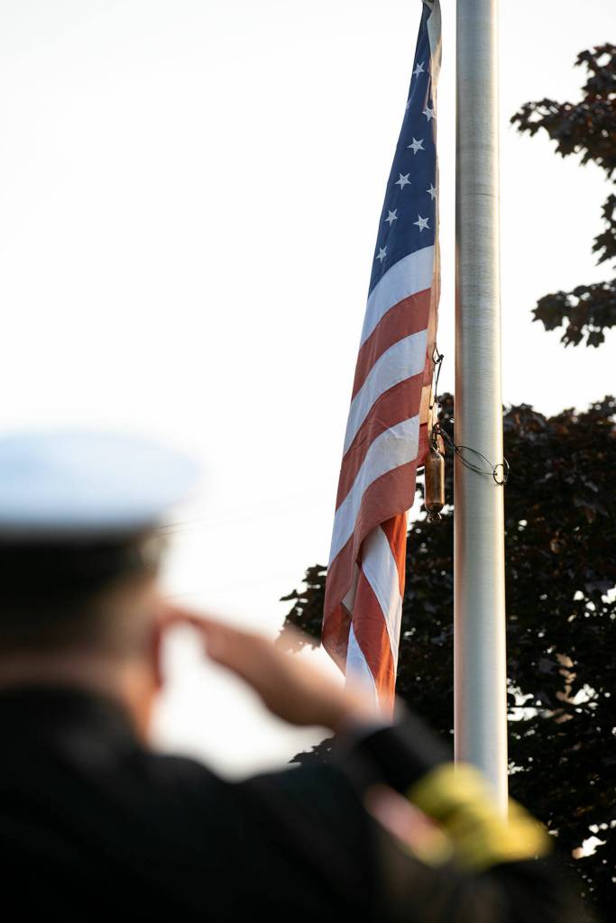 Firefighters stand and salute as the flag is lowered to half staff during a ceremony to commemorate the 21st anniversary of the September 11 terrorist attacks on the U.S. on Sep. 11, 2022, outside South County Fire Station 17 in downtown Edmonds, Washington. (Ryan Berry / The Herald)