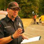 Snohomish Regional Fire & Rescue spokesperson Peter Mongillo speaks with a reporter as a television crew reports on the Bolt Creek Fire in the background on Saturday, Sep. 10, 2022, at Zekes Drive In near Index, Washington. (Ryan Berry / The Herald)