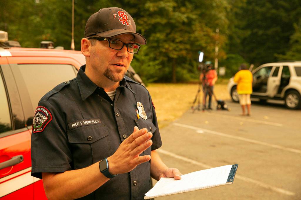 Snohomish Regional Fire & Rescue spokesperson Peter Mongillo speaks with a reporter as a television crew reports on the Bolt Creek Fire in the background on Saturday, Sep. 10, 2022, at Zekes Drive In near Index, Washington. (Ryan Berry / The Herald)