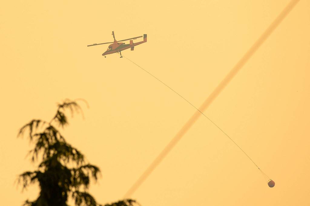 A firefighting helicopter carries a bucket of water from a nearby river to the Bolt Creek Fire on Saturday, Sep. 10, 2022, on U.S. Highway 2 near Index, Washington. (Ryan Berry / The Herald)