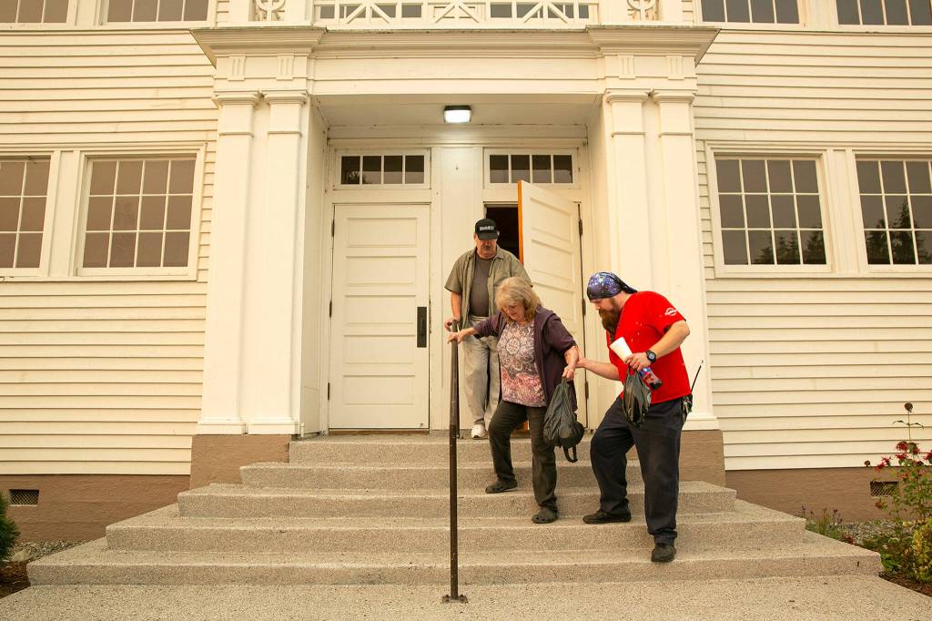 Trevor Meakin helps his mother Robyn and father Al down the steps of the Startup Event Center before making their way to Monroe in search for a hotel for them and there three cats after being displaced from their Baring home by the Bolt Creek Fire on Saturday, Sep. 10, 2022, in Startup, Washington. (Ryan Berry / The Herald)