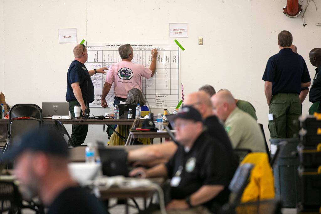Emergency responders from numerous agencies work together at the Bolt Creek Fire incident command inside a barn on Sunday, Sep. 11, 2022, at the Evergreen State Fairgrounds in Monroe, Washington. (Ryan Berry / The Herald)