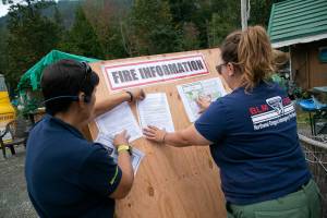 Public information officers Elizabeth Shepard and Lauren Woras put up an informational board regarding the Bolt Creek Fire outside of The Sand Bar Tavern at the intersection of U.S. 2 and Index-Galena Road on Wednesday, Sep. 14, 2022, in Index, Washington. (Ryan Berry / The Herald)