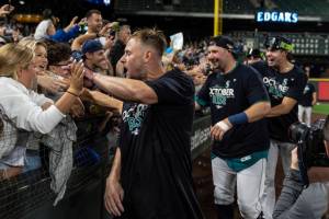 Seattle Mariners, including Jarred Kelenic, foreground, Cal Raleigh, second from left, and another player celebrate with fans after the team's baseball game against the Oakland Athletics, Friday, Sept. 30, 2022, in Seattle. The Mariners won 2-1 to clinch a spot in the playoffs. (AP Photo/Stephen Brashear)
