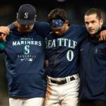 Seattle Mariners' Sam Haggerty, center, is helped off the field by training personnel manager Scott Servais, left, while stealing second base during the ninth inning of a baseball game against the Detroit Tigers, Monday, Oct. 3, 2022, in Seattle. The Tigers won 4-3. (AP Photo/Stephen Brashear)