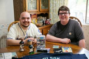 Mariners fans James Muramoto, 29 and brother Matt Kopp, 23, sit at the dining room table at their family’s home on Thursday, Oct. 5, 2022, in Everett, Washington. Muramoto said he has been a lifelong Mariners fan thanks to the passion of his late grandmother Edie Galen. (Ryan Berry / The Herald)