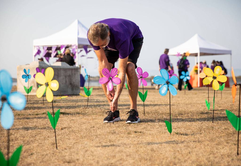 Rob Arbuckle puts a flower in the ground to remember his father Bob on Saturday during the annual Walk to End Alzheimers at Boxcar Park in Everett. (Olivia Vanni / The Herald)