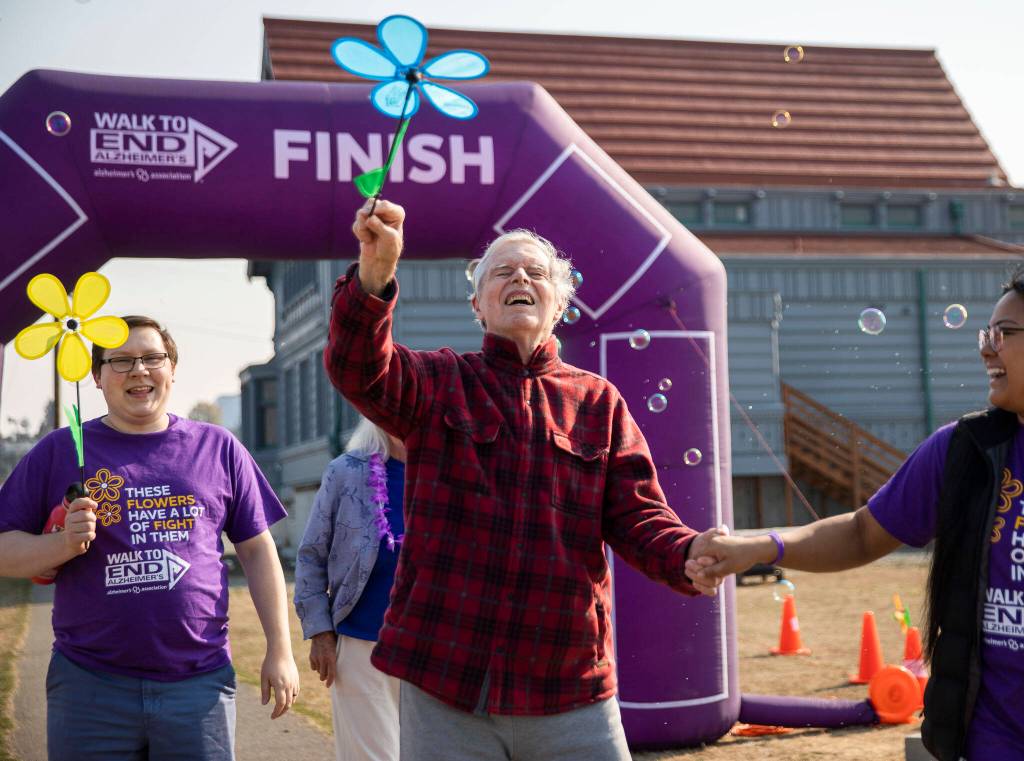 Merril Coulson, who has signs of both dementia and alzheimers, smiles Saturday while walking with one of his caregivers during the annual Walk to End Alzheimers at Boxcar Park in Everett. (Olivia Vanni / The Herald)
