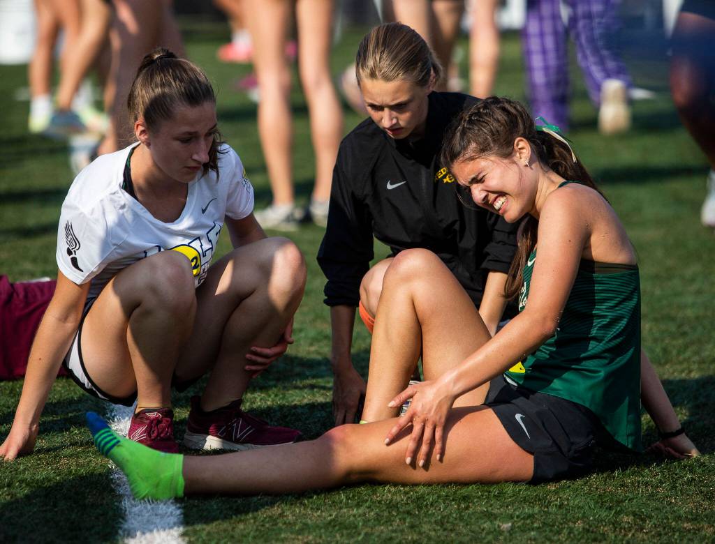 A runner grimaces and grabs their knee after finishing their race at the Hole In The Wall Invitational on Saturday, Oct. 8, 2022 in Arlington, Washington. (Olivia Vanni / The Herald)