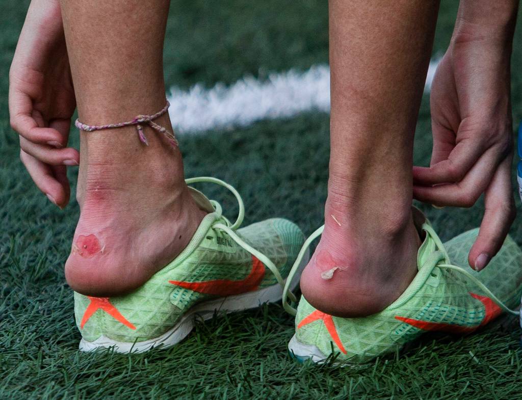 A runner pulls off their spiked shoes to relieve blisters on the back of their heels at the Hole In The Wall Invitational on Saturday, Oct. 8, 2022 in Arlington, Washington. (Olivia Vanni / The Herald)