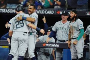 Seattle Mariners' Cal Raleigh (29) celebrates with Julio Rodriguez after scoring against the Toronto Blue Jays on a double by Adam Frazier, as J.P. Crawford, right, reacts during the ninth inning of Game 2 of a baseball AL wild-card playoff series Saturday, Oct. 8, 2022, in Toronto. (Nathan Denette/The Canadian Press via AP)