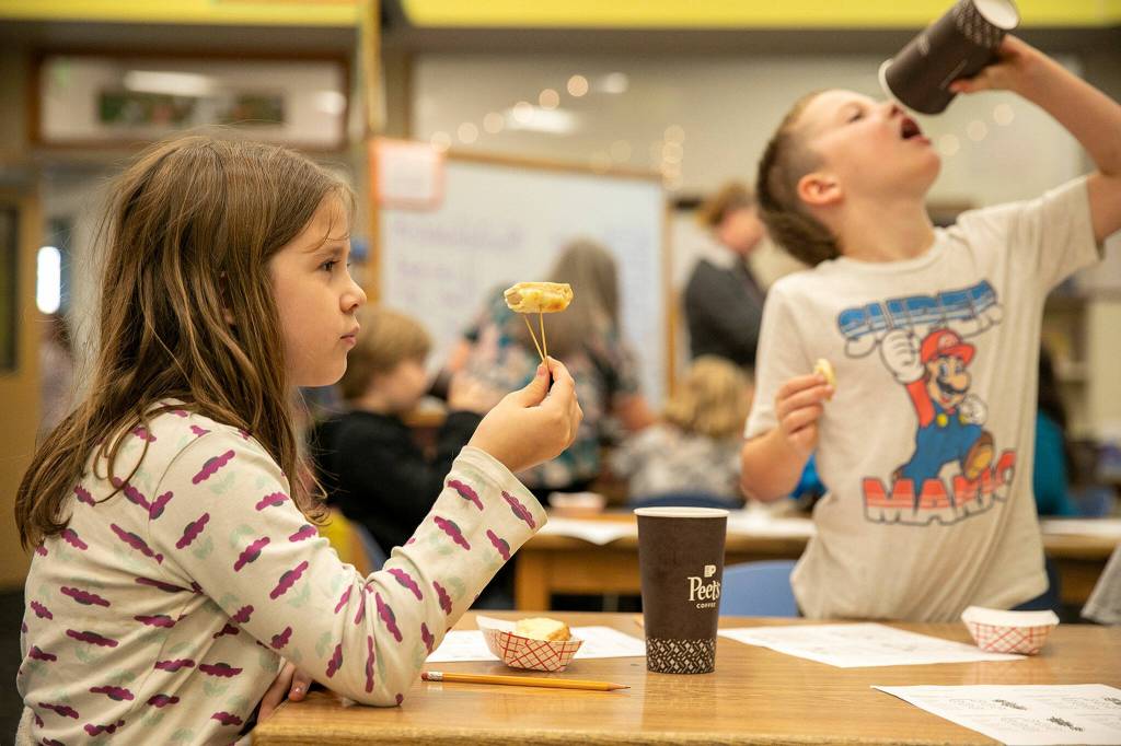 Third grader Melora Hoelscher takes a look at a garlic bread sample before giving it a taste Tuesday, at Eagle Creek Elementary, in Arlington. (Ryan Berry / The Herald)