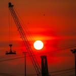 The sun turns a deep red as it sets beyond the Port of Everett and the Olympic Mountains on a hazardously smoky evening Sunday, Oct. 16, 2022, in Everett, Washington. (Ryan Berry / The Herald)