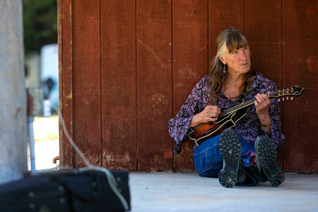 Tamara Kittredge, of Vashon, sits out back of the concession stand and noodles with a mandolin on July 13, at Darrington Bluegrass Music Park in Darrington. (Ryan Berry / The Herald)