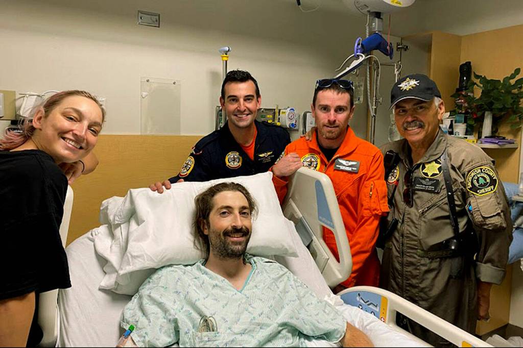 Snohomish County Helicopter Rescue Team, from left, Jeff Brown, Ryan Fleming and Bill Quistorf visit Benedict Delahunty and his partner, Missy Westland, on Oct. 18 at Harborview Medical Center in Seattle. (Snohomish County Helicopter Rescue Team)