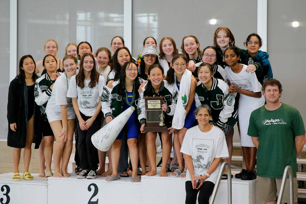 The Jackson High girls swim team pose for parent photos after winning the Class 4A District 1 swim meet Saturday, Nov. 5, 2022, at Snohomish Aquatic Center in Snohomish, Washington. (Ryan Berry / The Herald)