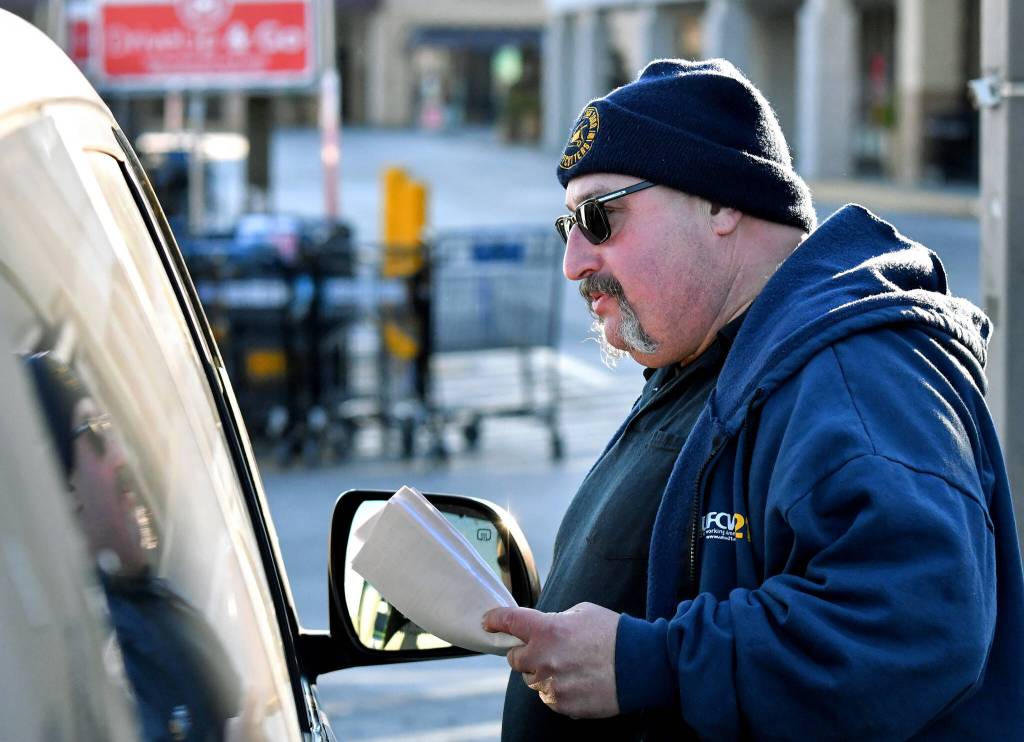 Kevin Flynn, a meat-cutter with the Marysville Albertsons, speaks with a passenger in a vehicle during a leaflet campaign on Wednesday, Nov. 9, 2022. Flynn was one of about a dozen grocery store workers handing out leaflets to shoppers about the proposed merger between Albertsons and Kroger. (Mike Henneke / The Herald)