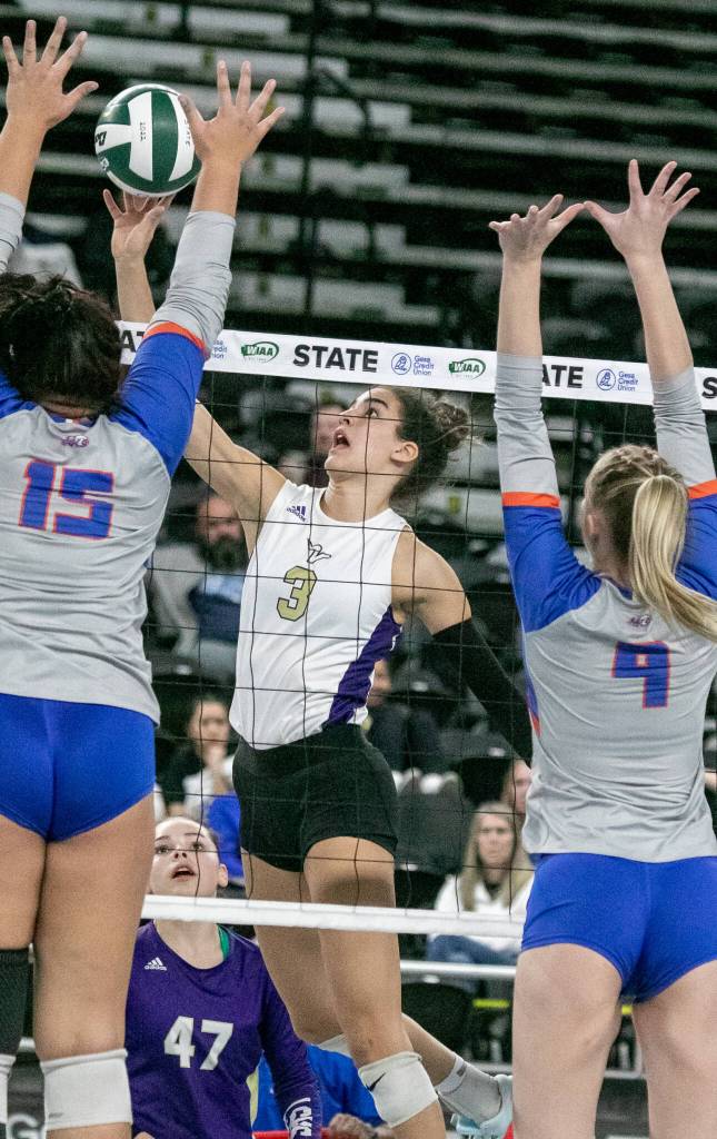 Lake Stevens Laura Eichert (3) hits between Graham-Kapowsins Hailey Brockway (15) and Grace Peterson (4) during the WIAA state volleyball championship on Saturday, Nov. 19, 2022, at the Yakima Valley SunDome. (TJ Mullinax/ For The Herald)