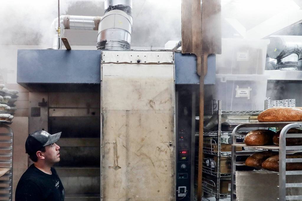 Conor ONeill watches steam rising from his decked oven Friday morning at The Cottage Community Bakery on Sept. 30, in Edmonds. (Kevin Clark / The Herald)