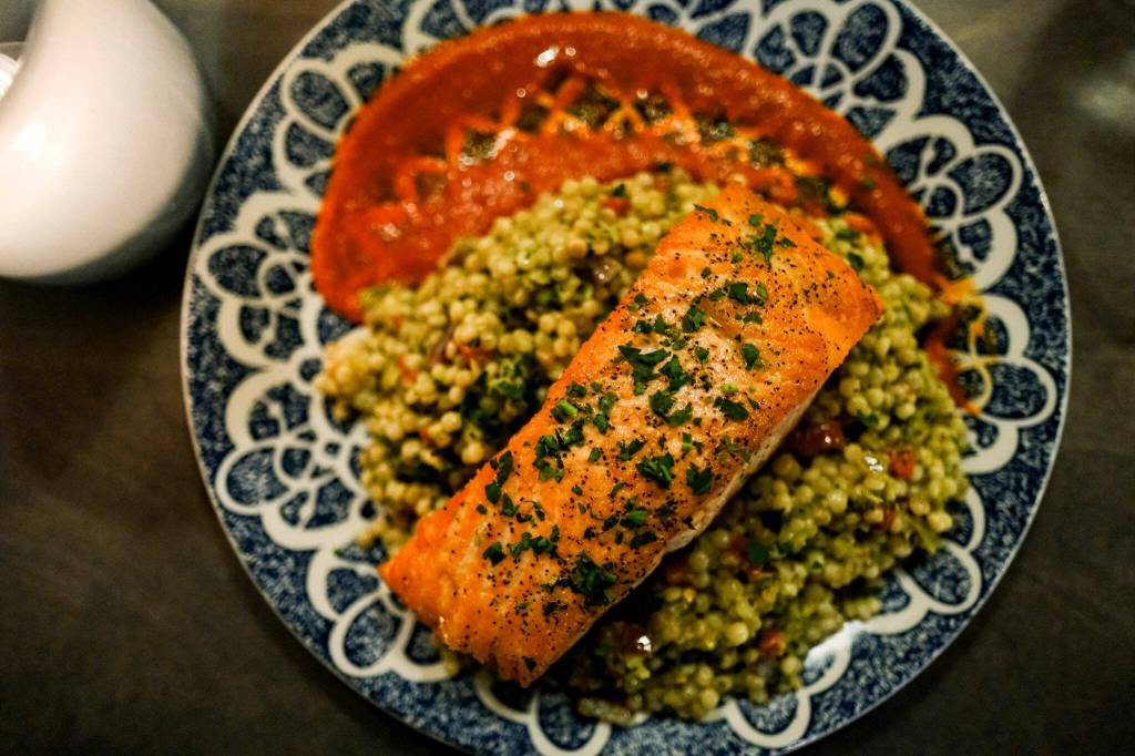 The salmon main at Salt & Iron in Edmonds achieves the dream balance of a tender-flaky interior with crispy skin all over. It is served atop brussels sprout pesto couscous, roasted red pepper and spicy arrabiata. (Taylor Goebel / The Herald)
