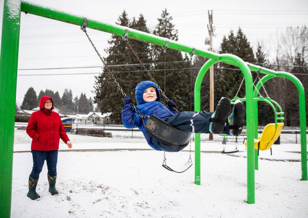 Hunter Clark, 3, smiles while his mom Heather Clark pushes him on a swing Tuesday as snow falls at Lundeen Park in Lake Stevens. (Olivia Vanni / The Herald)
