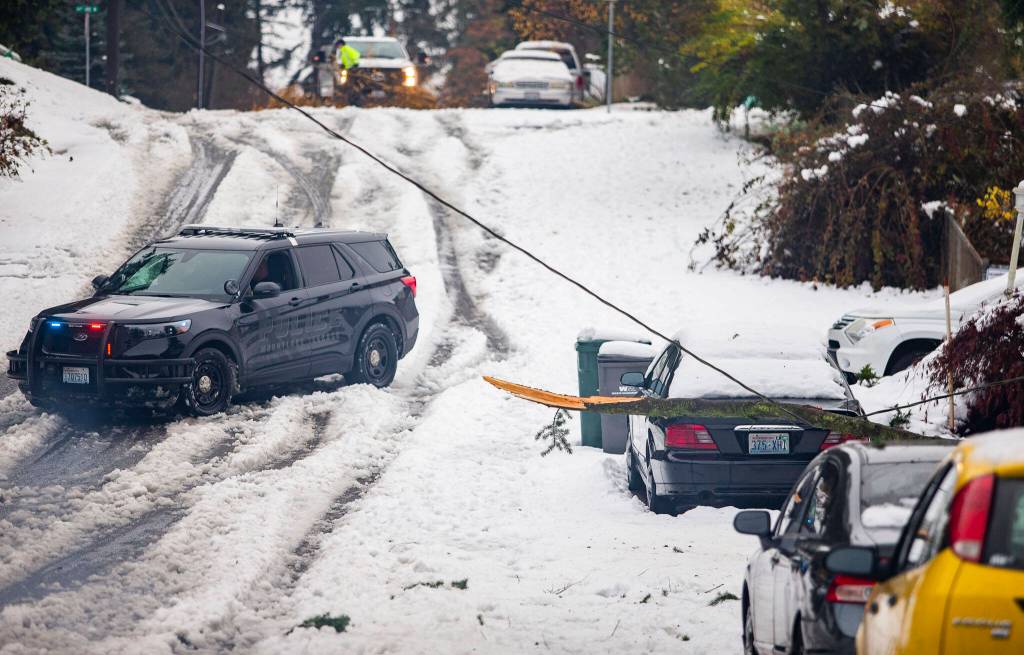 A Mountlake Terrace police officer blocks off a street with a live wire downed by a tree branch along 66th Avenue West on Wednesday, Nov. 30, 2022 in Mountlake Terrace, Washington. (Olivia Vanni / The Herald)