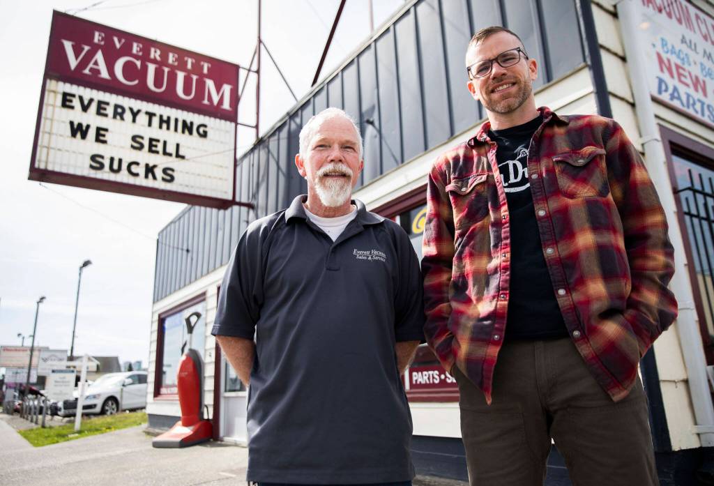 Father-and-son Mike and David Lane stand in front of Everett Vacuum on Broadway with their popular sign and saying, Everything we sell sucks. In November, the store moved to Hewitt Avenue, where overhang signs arent allowed, so a new flat banner with the sucks saying was made for the front window. (Olivia Vanni / The Herald)