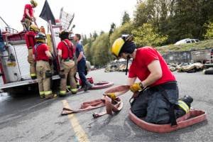 After a day of learning to fight fires, Snohomish firefighter recruit Chau Nguyen flakes a hose as other recruits load the hoses onto a fire truck April 19, 2018, at the training facility on S. Machias Rd. in Snohomish. (Andy Bronson / Herald file)