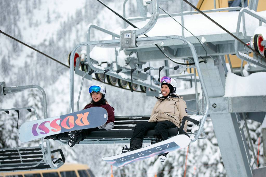 Two snowboarders head up the mountain in a lift chair. (Ryan Berry / The Herald)