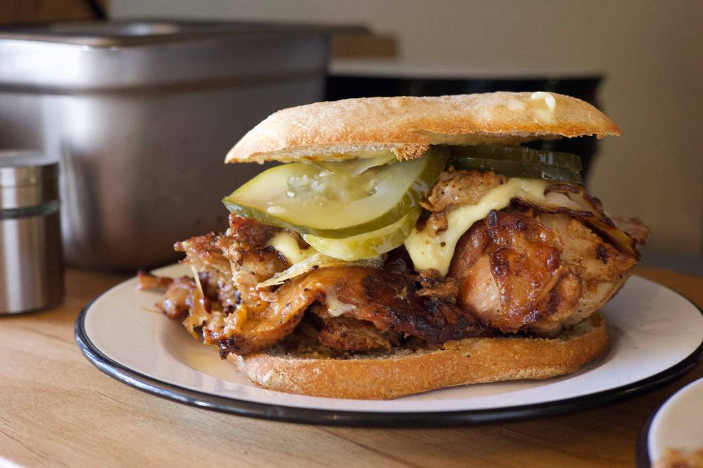 The Midnight Cuban sandwich is Maize & Barleys PNW take on a Miami classic: chunks of house-smoked, slow roasted pork shoulder and loin, white cheese, house pickles, mustard and vegan aioli practically burst out of thin slices of ciabatta. (Photo courtesy of Venus Forteza).